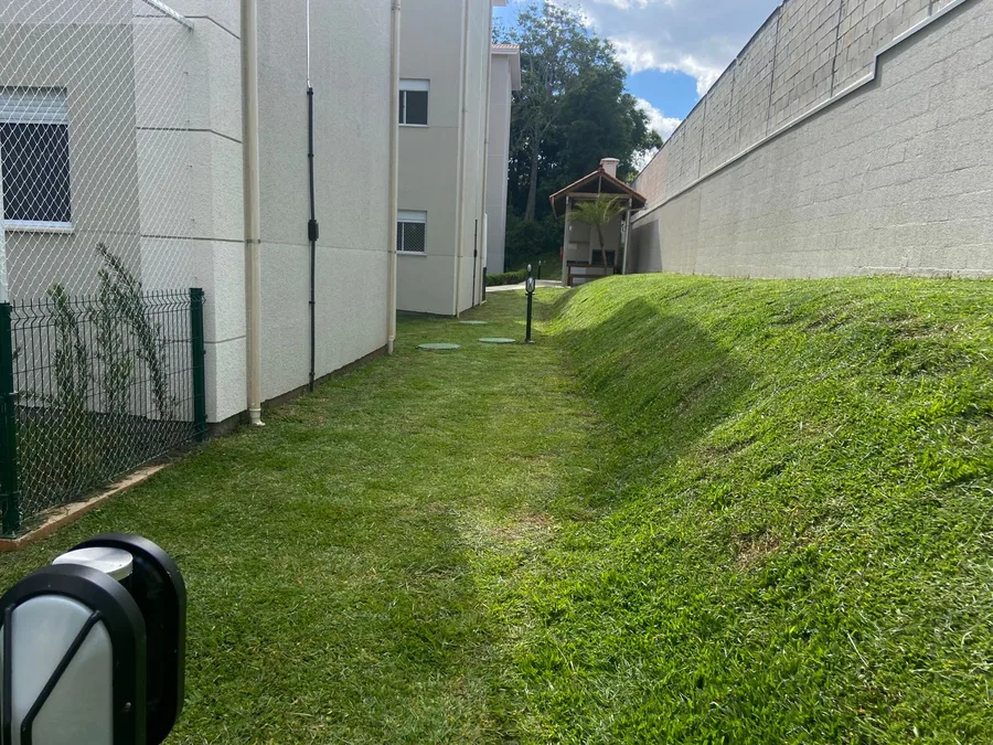Área gramada junto aos blocos residenciais e ao muro do condomínio.